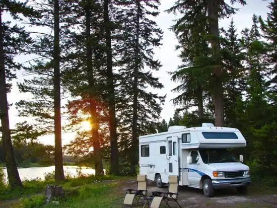 RV parked next to lake with two chairs next to it