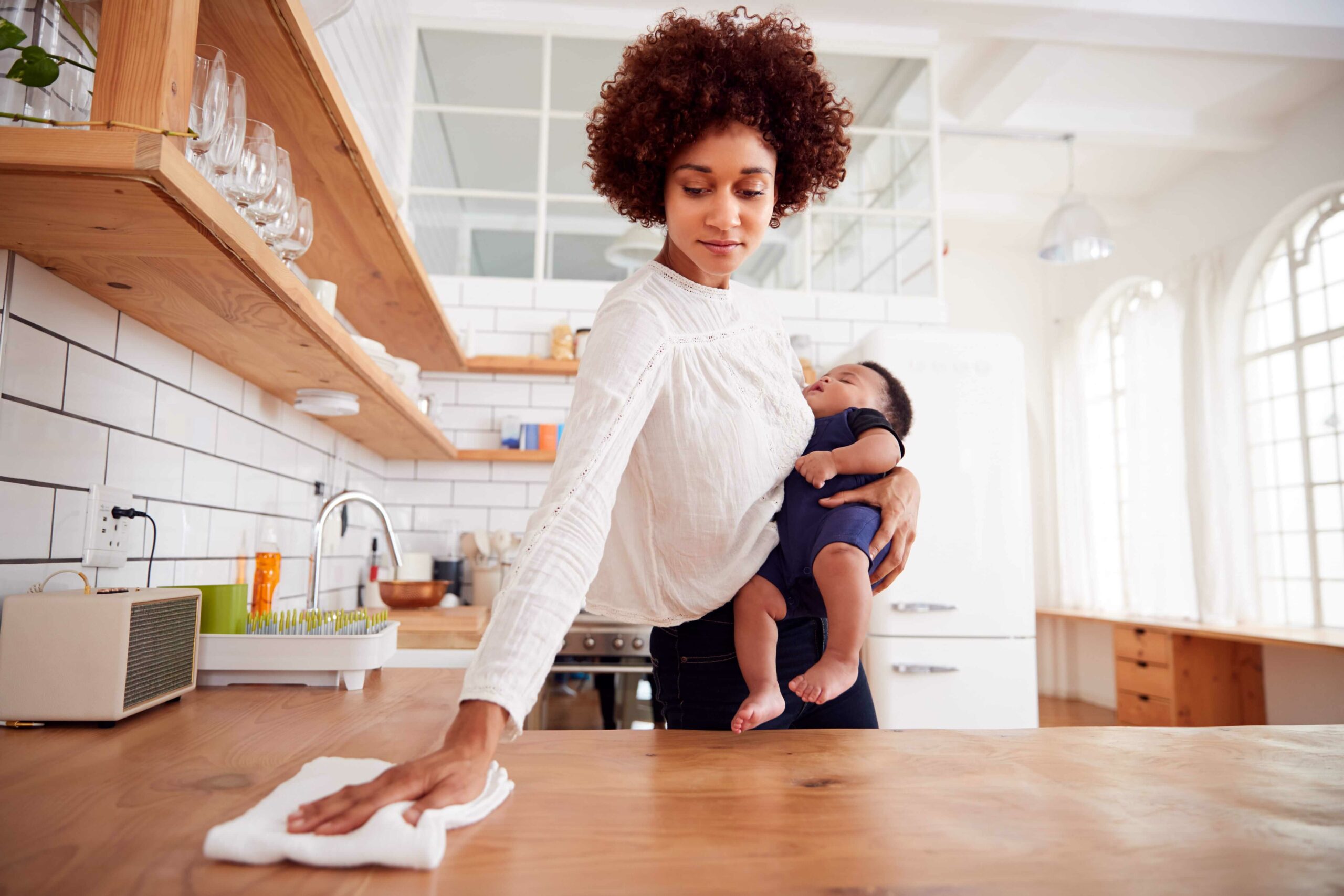 Woman holding baby and cleaning up crumbs off counter
